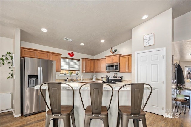 kitchen featuring visible vents, lofted ceiling, appliances with stainless steel finishes, a kitchen breakfast bar, and a sink