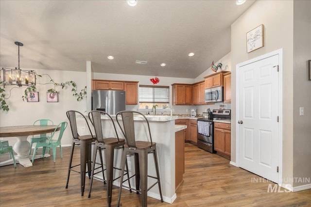 kitchen featuring a breakfast bar area, stainless steel appliances, wood finished floors, a kitchen island, and brown cabinets