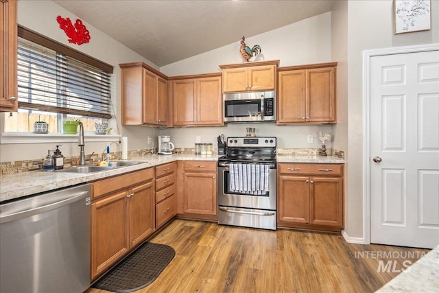 kitchen with appliances with stainless steel finishes, lofted ceiling, a sink, and light wood-style flooring