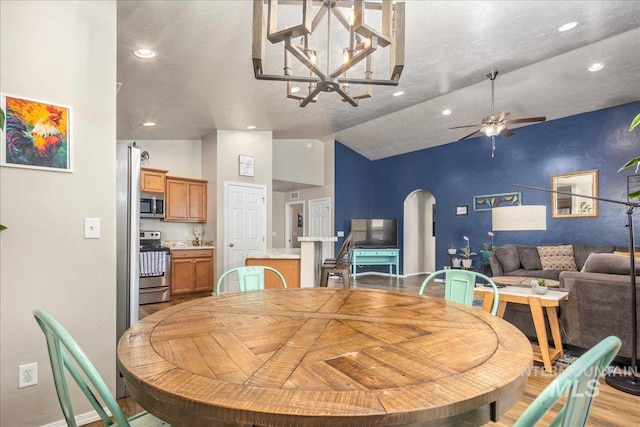 dining area featuring arched walkways, recessed lighting, ceiling fan with notable chandelier, light wood-style floors, and vaulted ceiling