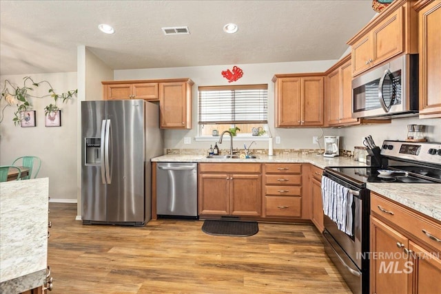 kitchen with stainless steel appliances, a sink, visible vents, light wood-type flooring, and brown cabinetry