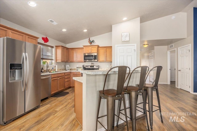 kitchen with visible vents, lofted ceiling, appliances with stainless steel finishes, light wood-style floors, and a kitchen bar