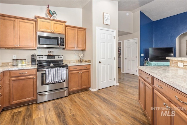 kitchen with lofted ceiling, stainless steel appliances, brown cabinetry, and wood finished floors