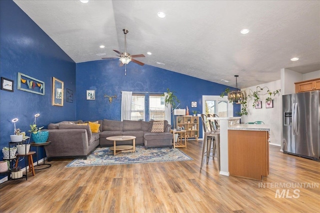 living room with lofted ceiling, a textured ceiling, ceiling fan with notable chandelier, wood finished floors, and baseboards