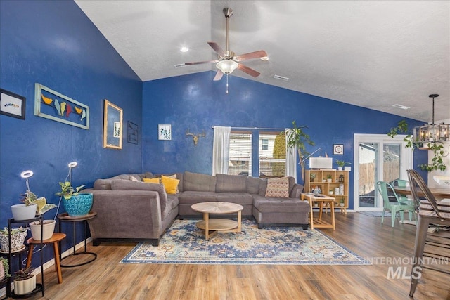 living area with lofted ceiling, ceiling fan with notable chandelier, wood finished floors, visible vents, and baseboards