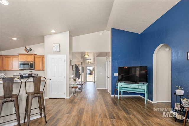 kitchen featuring arched walkways, stainless steel appliances, dark wood-type flooring, vaulted ceiling, and baseboards