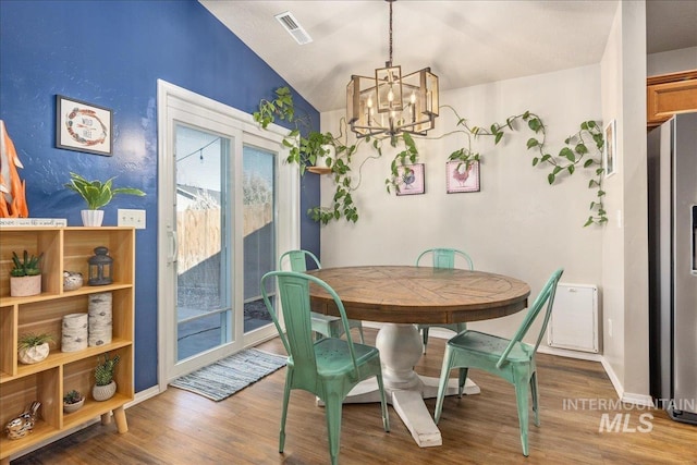 dining area with a notable chandelier, lofted ceiling, visible vents, wood finished floors, and baseboards