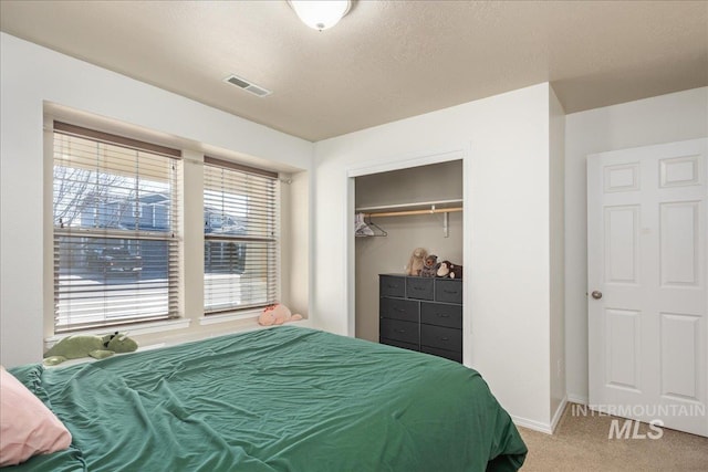 carpeted bedroom featuring a closet, visible vents, a textured ceiling, and baseboards