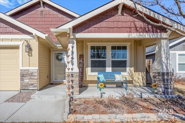 entrance to property featuring covered porch, stone siding, and a garage