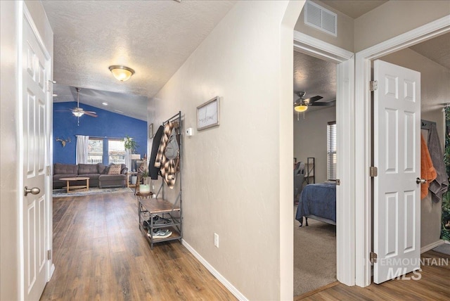 hallway featuring lofted ceiling, visible vents, a textured ceiling, wood finished floors, and baseboards