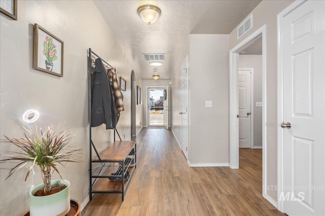 hall with visible vents, a textured ceiling, baseboards, and wood finished floors