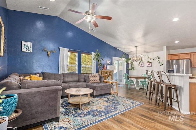 living area with visible vents, lofted ceiling, wood finished floors, a textured ceiling, and ceiling fan with notable chandelier