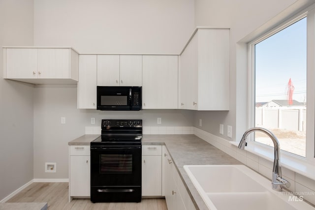 kitchen featuring a wealth of natural light, white cabinets, black appliances, and light hardwood / wood-style floors
