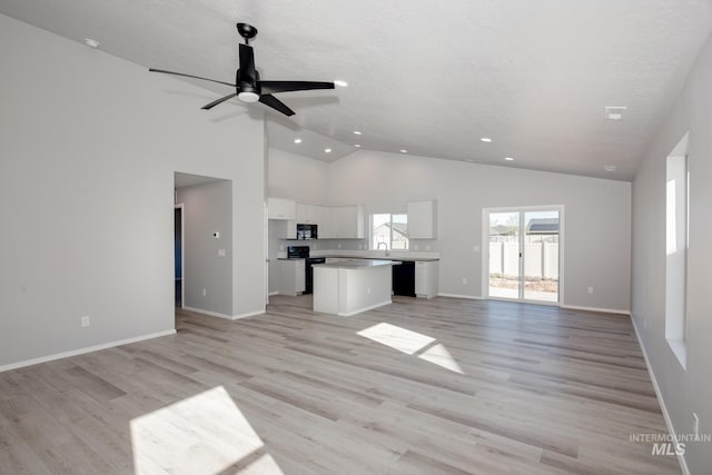 unfurnished living room with high vaulted ceiling, ceiling fan, light hardwood / wood-style flooring, and sink