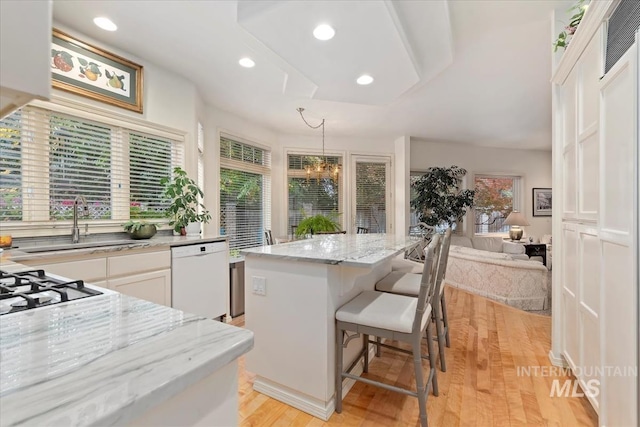 kitchen featuring white cabinetry, dishwasher, a kitchen breakfast bar, pendant lighting, and a kitchen island