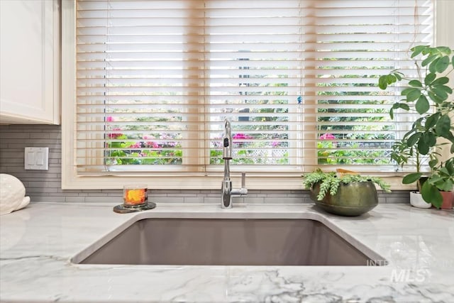 room details with white cabinets, light stone counters, and sink