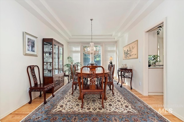 dining space featuring light wood-type flooring, a raised ceiling, and a notable chandelier