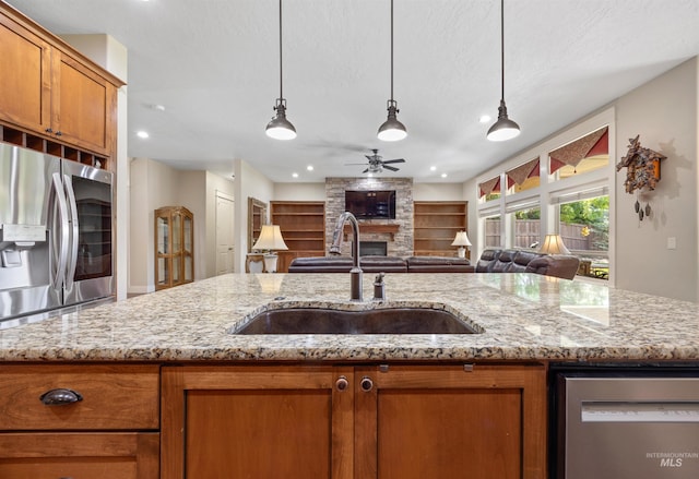 1573 E Commander St, Meridian, ID 83646 - kitchen with a stone fireplace, stainless steel appliances, a sink, brown cabinetry, and open floor plan