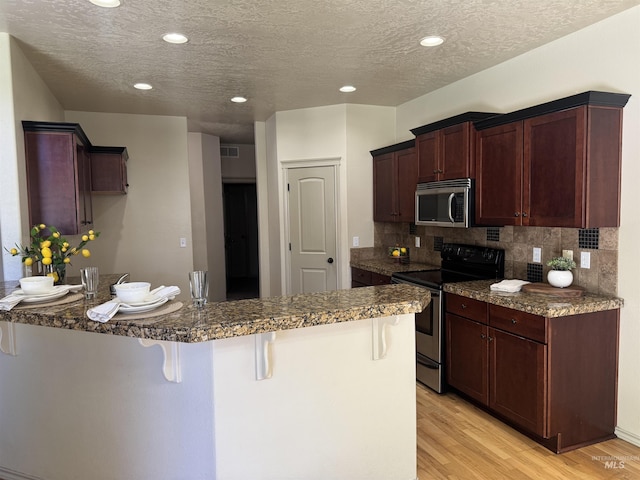 3669 N Dixon Ave, Meridian, ID 83646 - kitchen with appliances with stainless steel finishes, a breakfast bar area, a peninsula, decorative backsplash, and light wood-type flooring