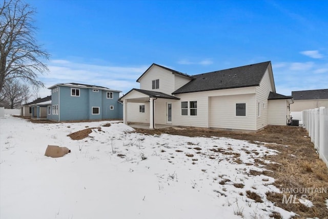 snow covered house with a garage, cooling unit, and fence