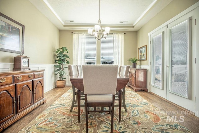 dining area with a tray ceiling, a wainscoted wall, and light wood finished floors