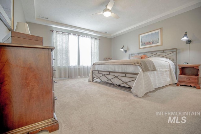 bedroom featuring carpet floors, a raised ceiling, visible vents, and ceiling fan