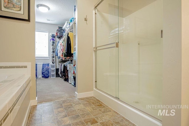 full bath with a stall shower, a walk in closet, a textured ceiling, and baseboards