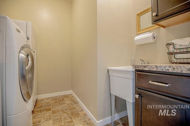 clothes washing area with stone finish floor, washer / dryer, cabinet space, and baseboards