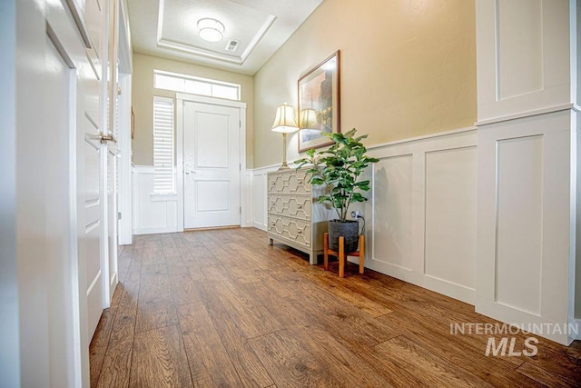 entryway with visible vents, wainscoting, wood-type flooring, a tray ceiling, and a decorative wall