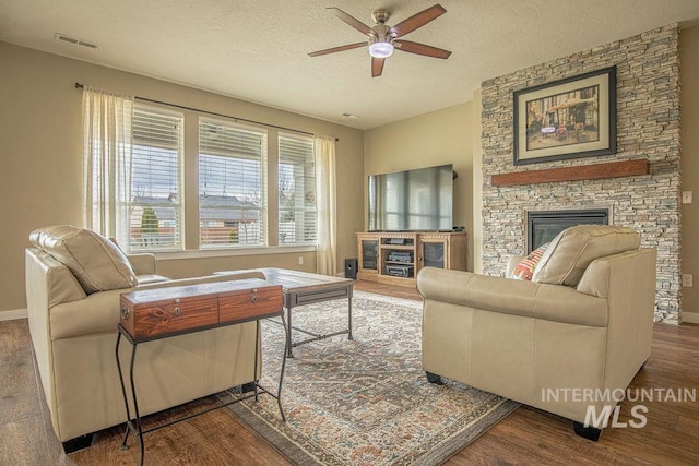 living area featuring a textured ceiling, a fireplace, visible vents, and wood finished floors