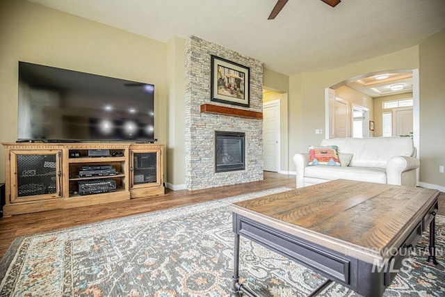 living room with baseboards, a ceiling fan, wood finished floors, and a stone fireplace