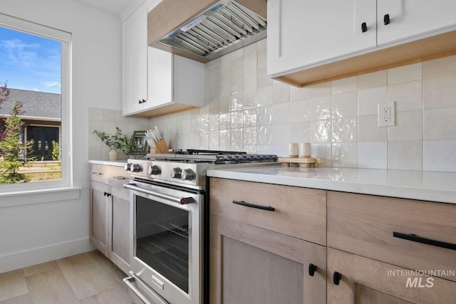 kitchen featuring high end range, a healthy amount of sunlight, white cabinetry, and wall chimney exhaust hood