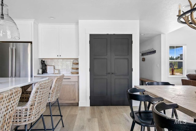 kitchen featuring an inviting chandelier, white cabinets, decorative backsplash, light wood-type flooring, and high quality fridge