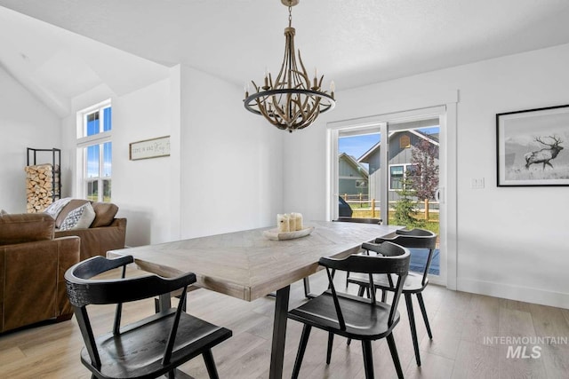 dining space featuring light wood-type flooring, an inviting chandelier, and lofted ceiling