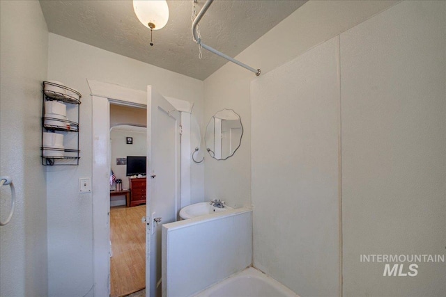 full bathroom featuring a textured ceiling, wood finished floors, and a washtub