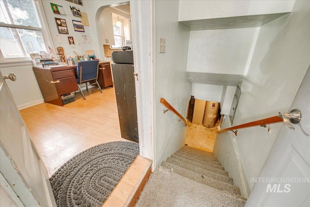 stairs featuring arched walkways and wood finished floors