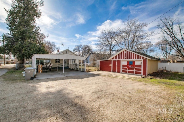 view of outdoor structure with a carport, an outdoor structure, dirt driveway, and fence