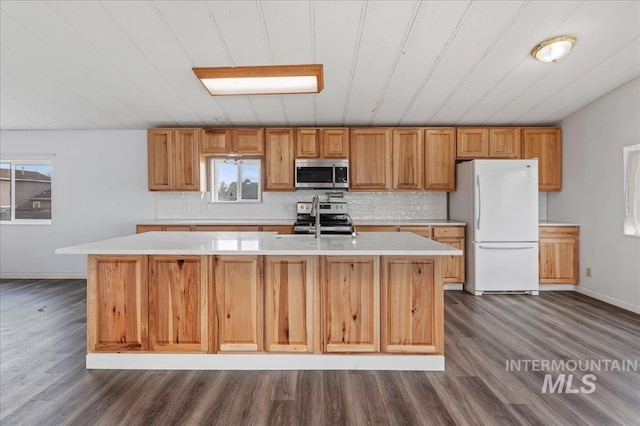 kitchen featuring an island with sink, dark wood-style floors, appliances with stainless steel finishes, light countertops, and decorative backsplash