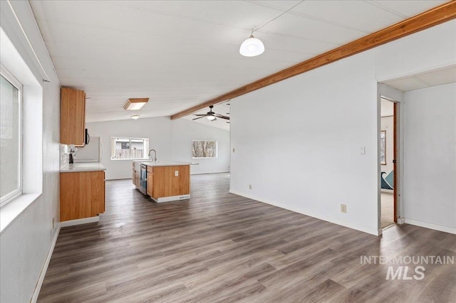 kitchen with vaulted ceiling with beams, open floor plan, light countertops, brown cabinets, and a sink