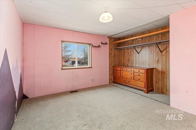 unfurnished bedroom with visible vents, wood walls, and carpet