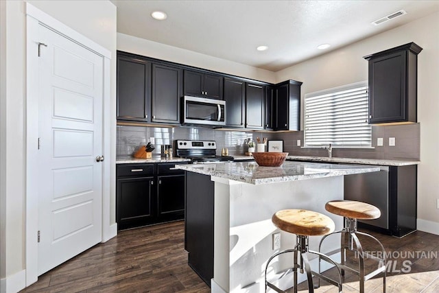 kitchen with a kitchen breakfast bar, stainless steel appliances, a center island, light stone countertops, and dark wood-type flooring