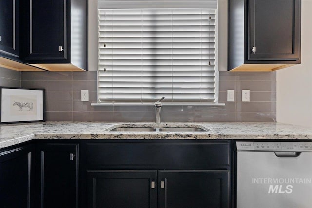 kitchen featuring light stone counters, stainless steel dishwasher, tasteful backsplash, and sink