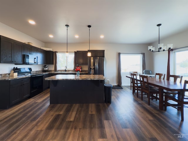 kitchen with electric range, a center island, stainless steel refrigerator with ice dispenser, decorative light fixtures, and dark stone counters