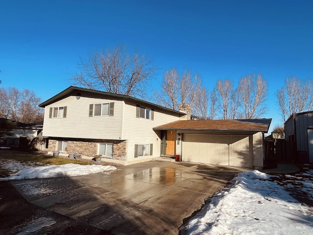 tri-level home with driveway, stone siding, a chimney, and an attached garage