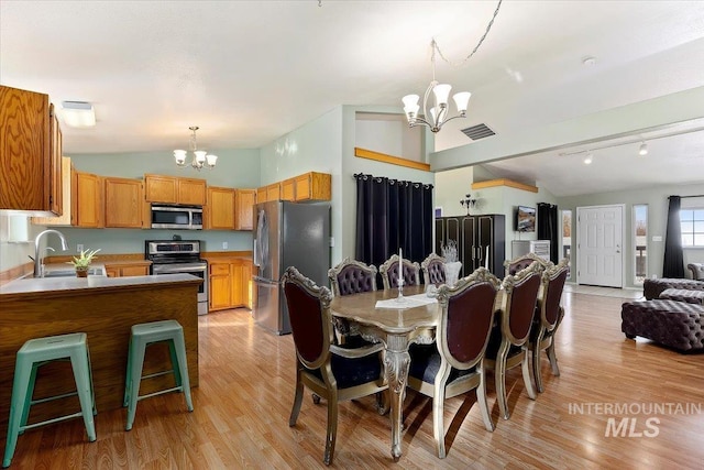 dining space with a notable chandelier, light hardwood / wood-style floors, vaulted ceiling, and sink