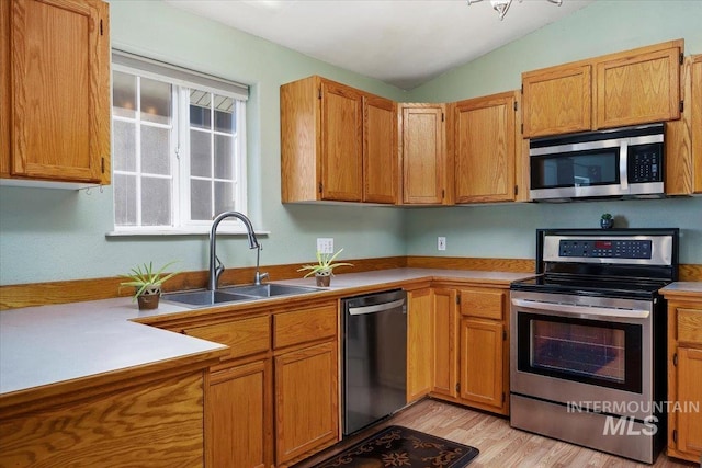 kitchen featuring appliances with stainless steel finishes, light hardwood / wood-style floors, vaulted ceiling, and sink