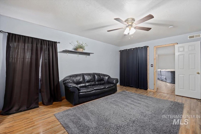 living area featuring ceiling fan, a textured ceiling, and wood-type flooring