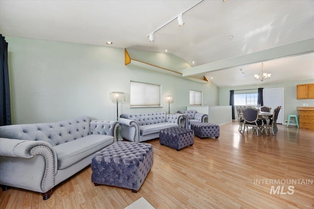 living room with lofted ceiling, rail lighting, a notable chandelier, and light hardwood / wood-style flooring