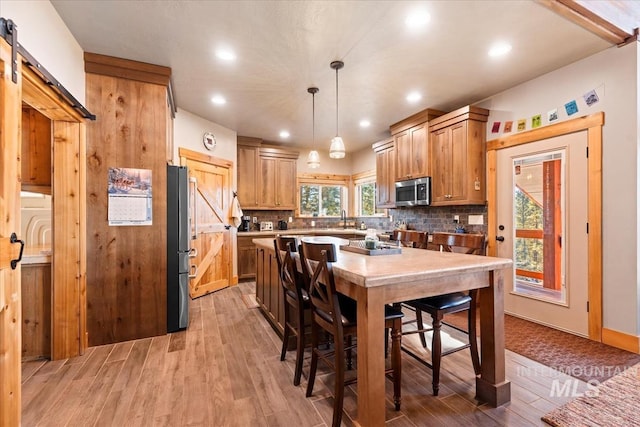 kitchen with tasteful backsplash, hanging light fixtures, a barn door, and appliances with stainless steel finishes