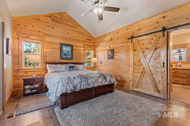 bedroom with lofted ceiling, hardwood / wood-style floors, multiple windows, and a barn door